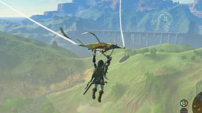 Screenshot of Link from The Legend of Zelda: Tears of the Kingdom. He is soaring over a grassy plain on his Tears of the Kingdom Paraglider.